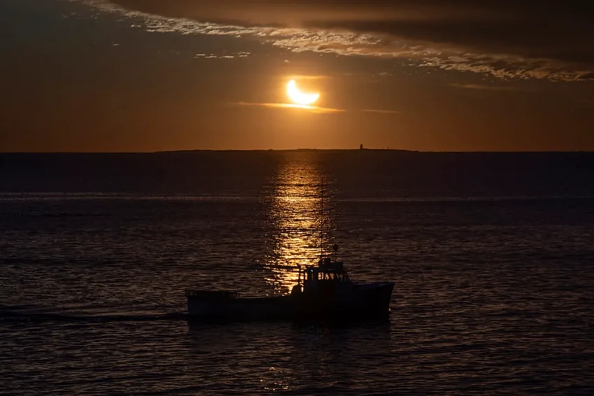 Partially eclipsed sun setting over the Atlantic off Porto, with a boat in silhouette