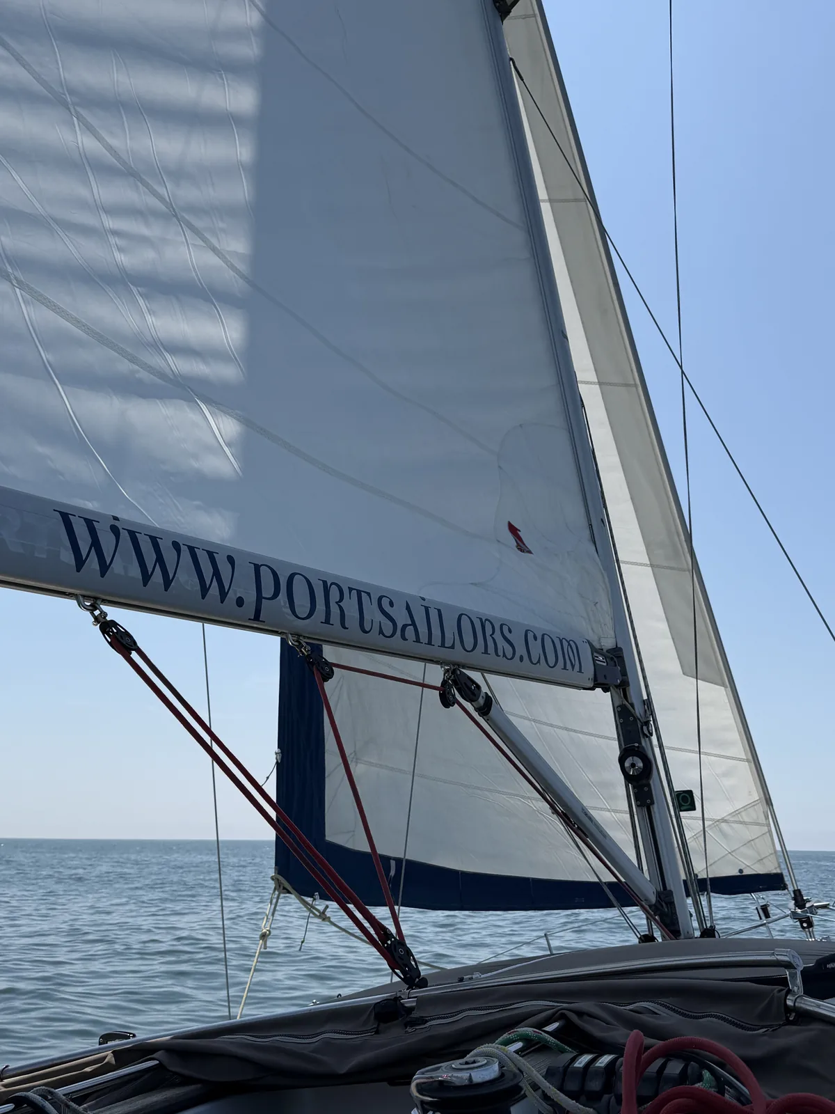 Full mainsail and jib set against a clear blue sky over open Atlantic water off Porto