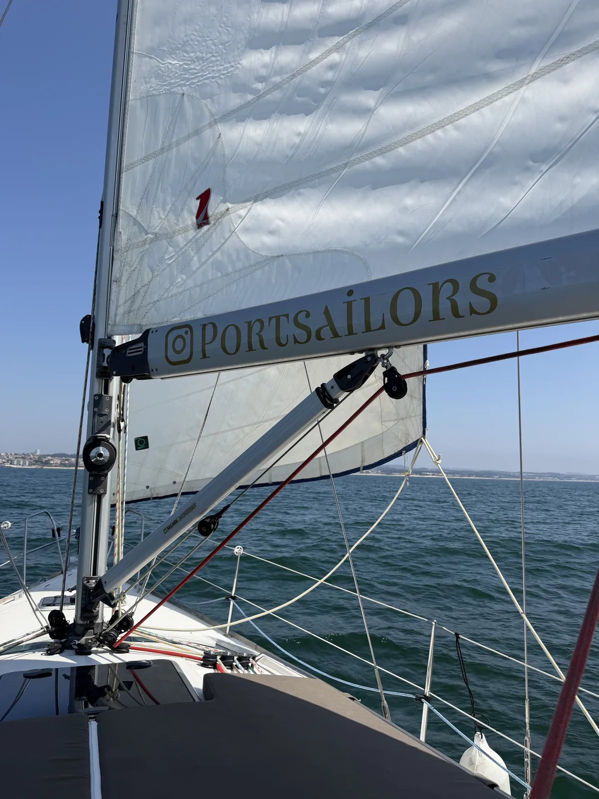 View forward over the bow of a Port Sailors sailboat under sail, the Porto coastline on the horizon