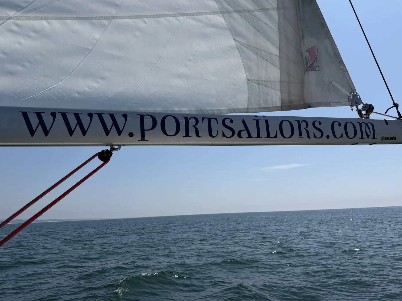 A sailboat boom marked www.portsailors.com over the Atlantic Ocean off Porto under full sail