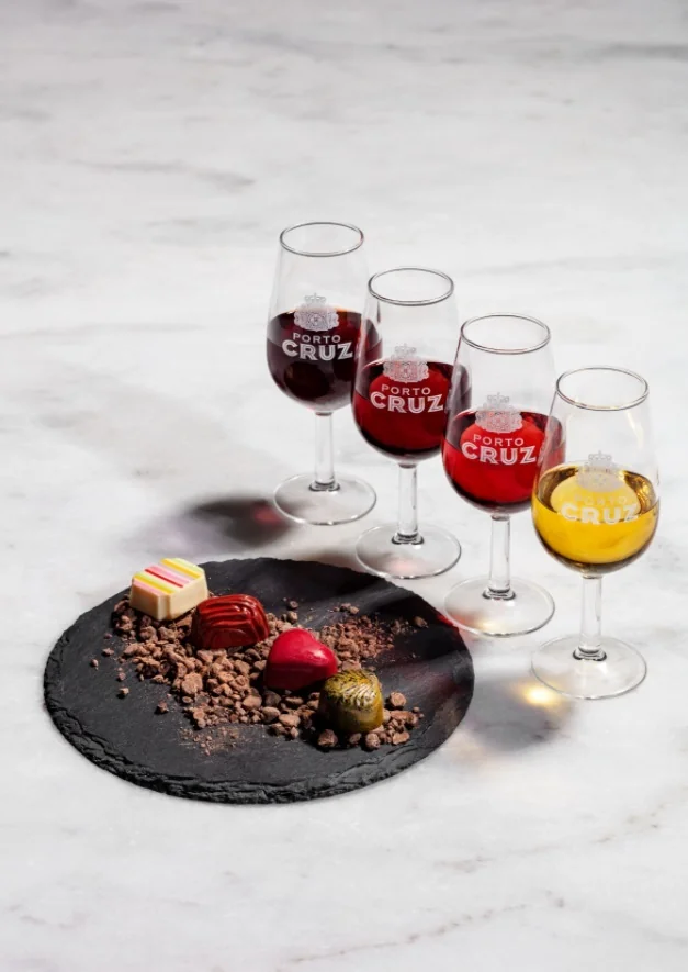 Four glasses of Port — red, tawny, rosé and white — beside artisan chocolate pralines on a slate plate