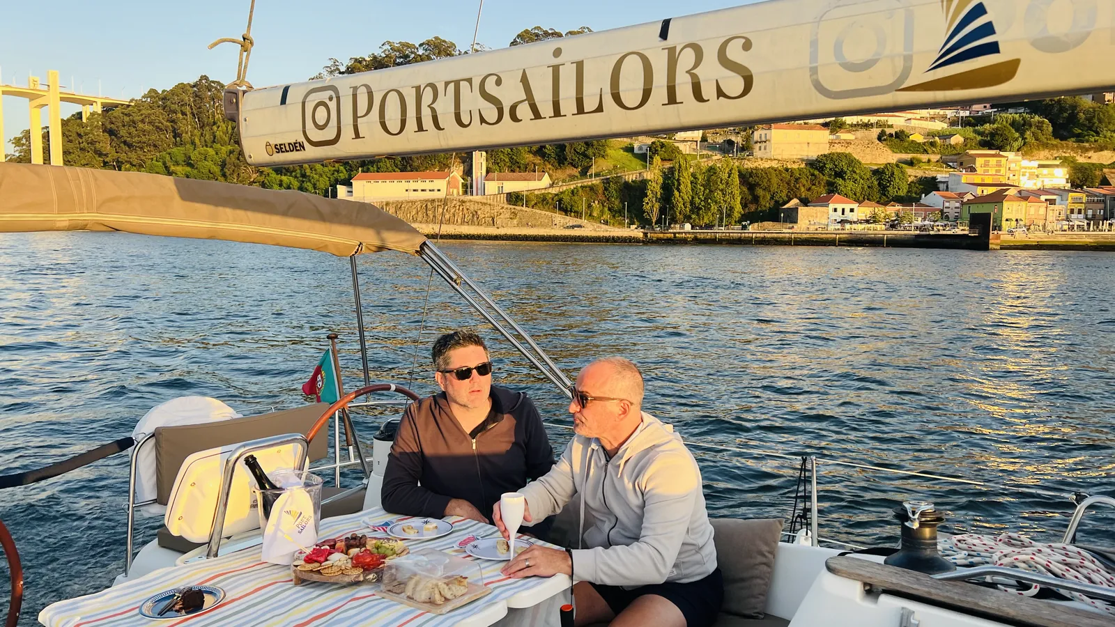 Couple enjoying lunch on deck as the sailboat passes under the Arrabida Bridge in Porto