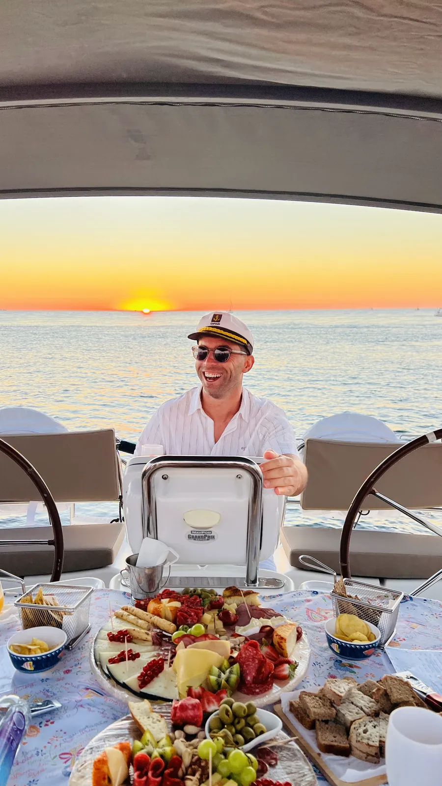 Smiling captain in a captain's hat at a charcuterie table on board at sunset in Porto