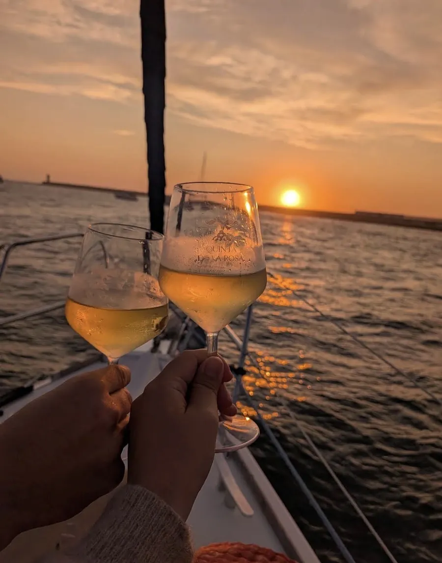 Two guests toasting rose wine as the sun sets over the Atlantic on a Porto sailing cruise
